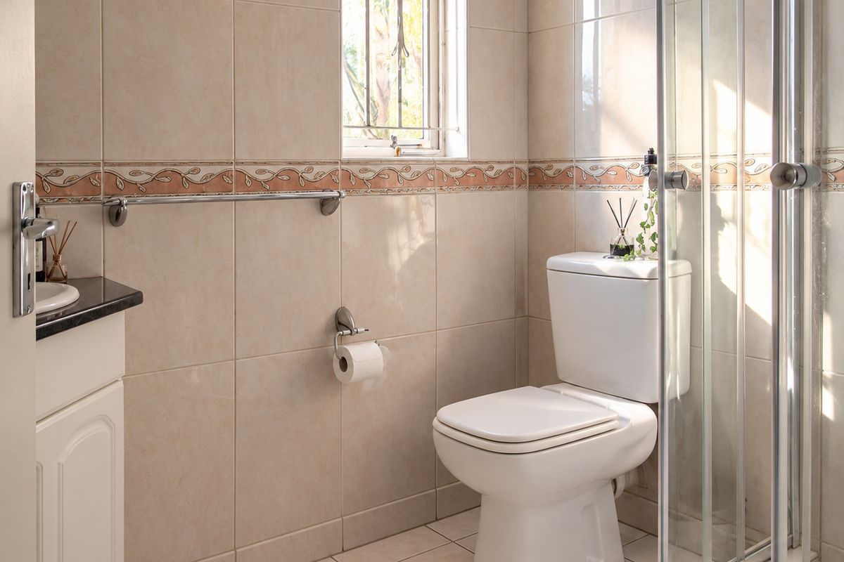 A functional bathroom featuring a vanity with granite countertop, a toilet, and a glass-enclosed shower, finished with neutral ceramic wall tiles.
