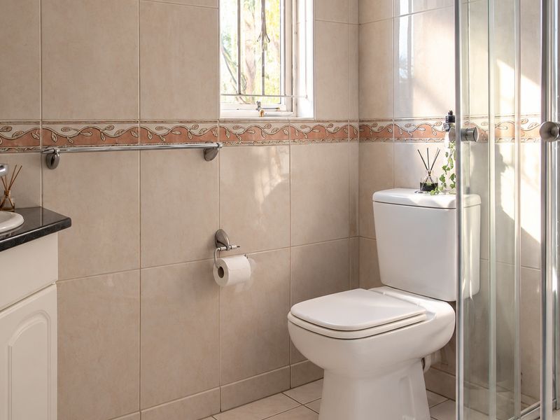 A functional bathroom featuring a vanity with granite countertop, a toilet, and a glass-enclosed shower, finished with neutral ceramic wall tiles.