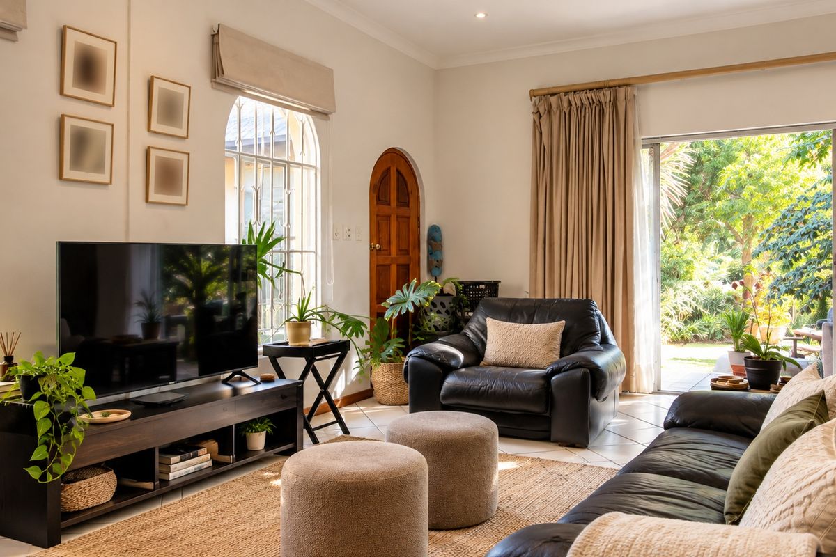A bright living room featuring arched windows with security bars, tiled flooring, and a sliding glass door providing direct access to the garden.