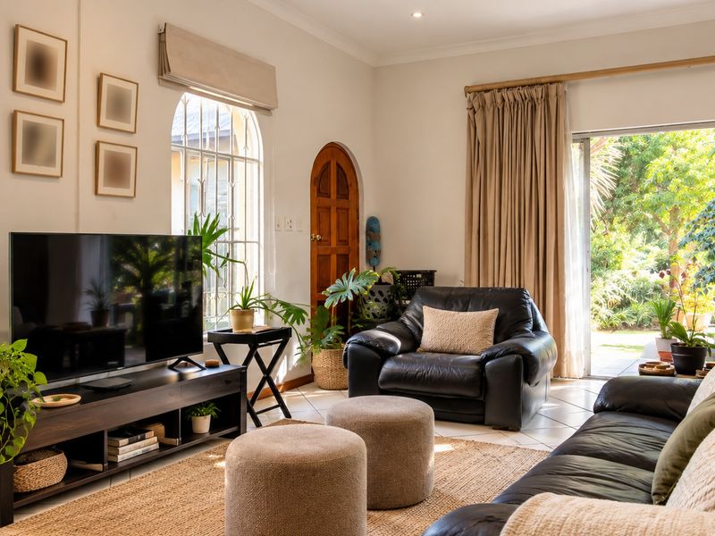 A bright living room featuring arched windows with security bars, tiled flooring, and a sliding glass door providing direct access to the garden.