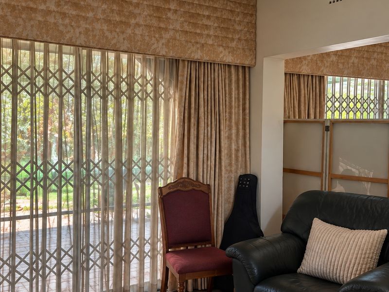 A living room area featuring large sliding glass doors with integrated security gates, complemented by decorative pelmets and floor-length curtains.