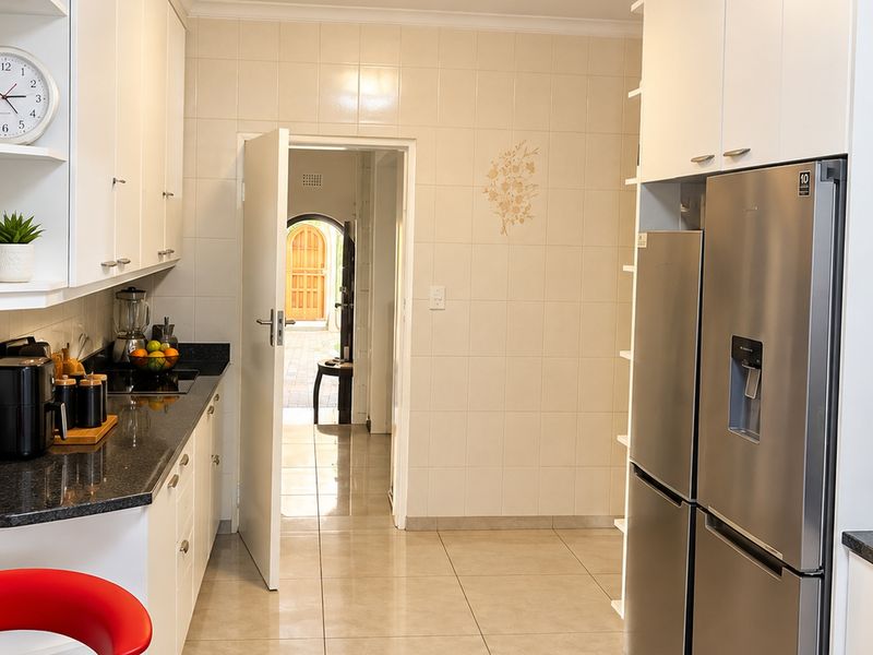 A functional kitchen featuring white cabinetry, dark granite countertops, tiled backsplash, and large format floor tiles, with a view through to the entrance.