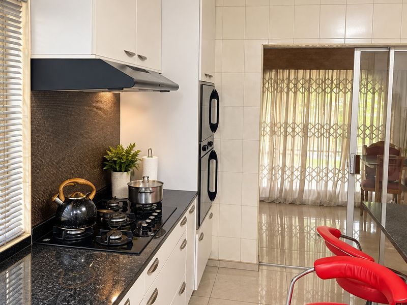 Modern kitchen featuring granite countertops, a gas hob with extractor fan, and a built-in double oven, leading through a sliding door to the dining area.