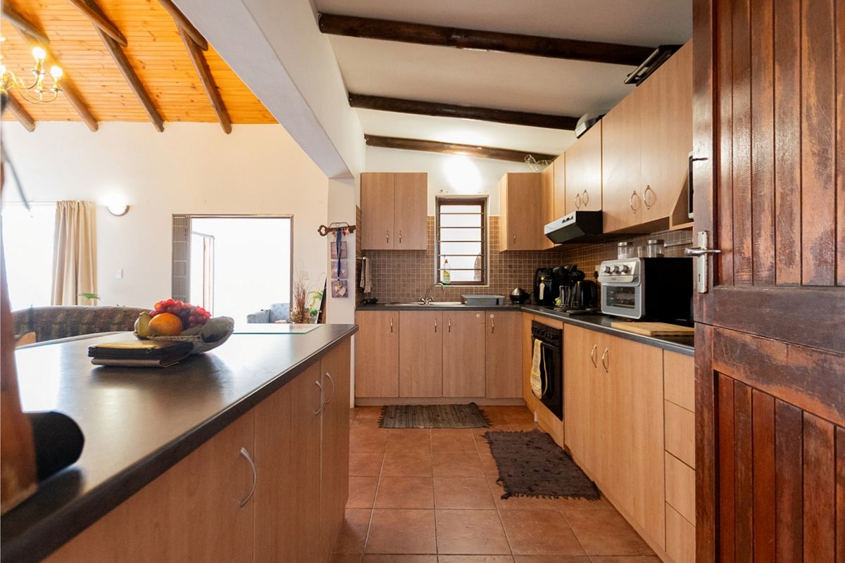 Functional kitchen featuring light wood cabinetry, dark countertops, tiled flooring, and exposed timber ceiling beams, seamlessly connected to the adjacent living area.