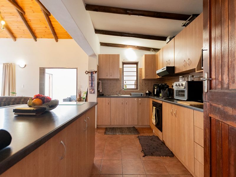 Functional kitchen featuring light wood cabinetry, dark countertops, tiled flooring, and exposed timber ceiling beams, seamlessly connected to the adjacent living area.