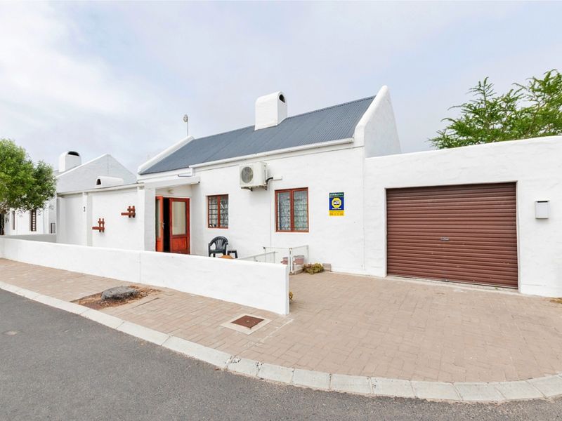Front elevation of a white cottage-style house featuring a corrugated metal roof, paved driveway, and an integrated garage with a roller door.