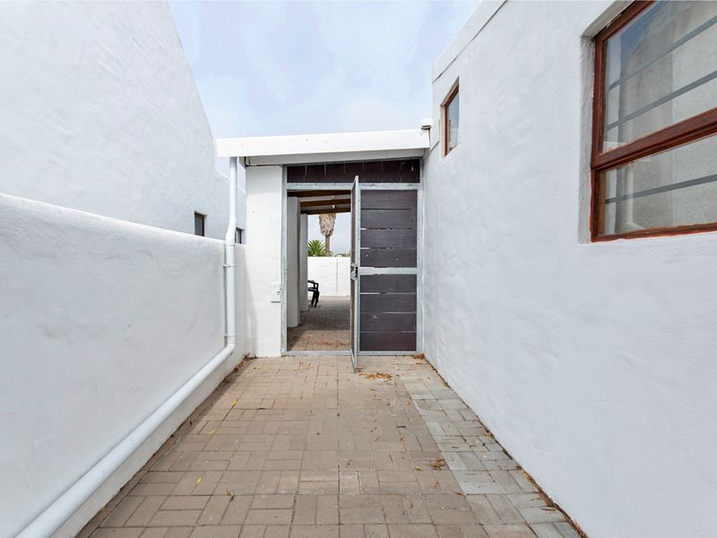 A narrow paved exterior walkway leading to a timber gate, featuring white rendered walls and a functional drainage downpipe.