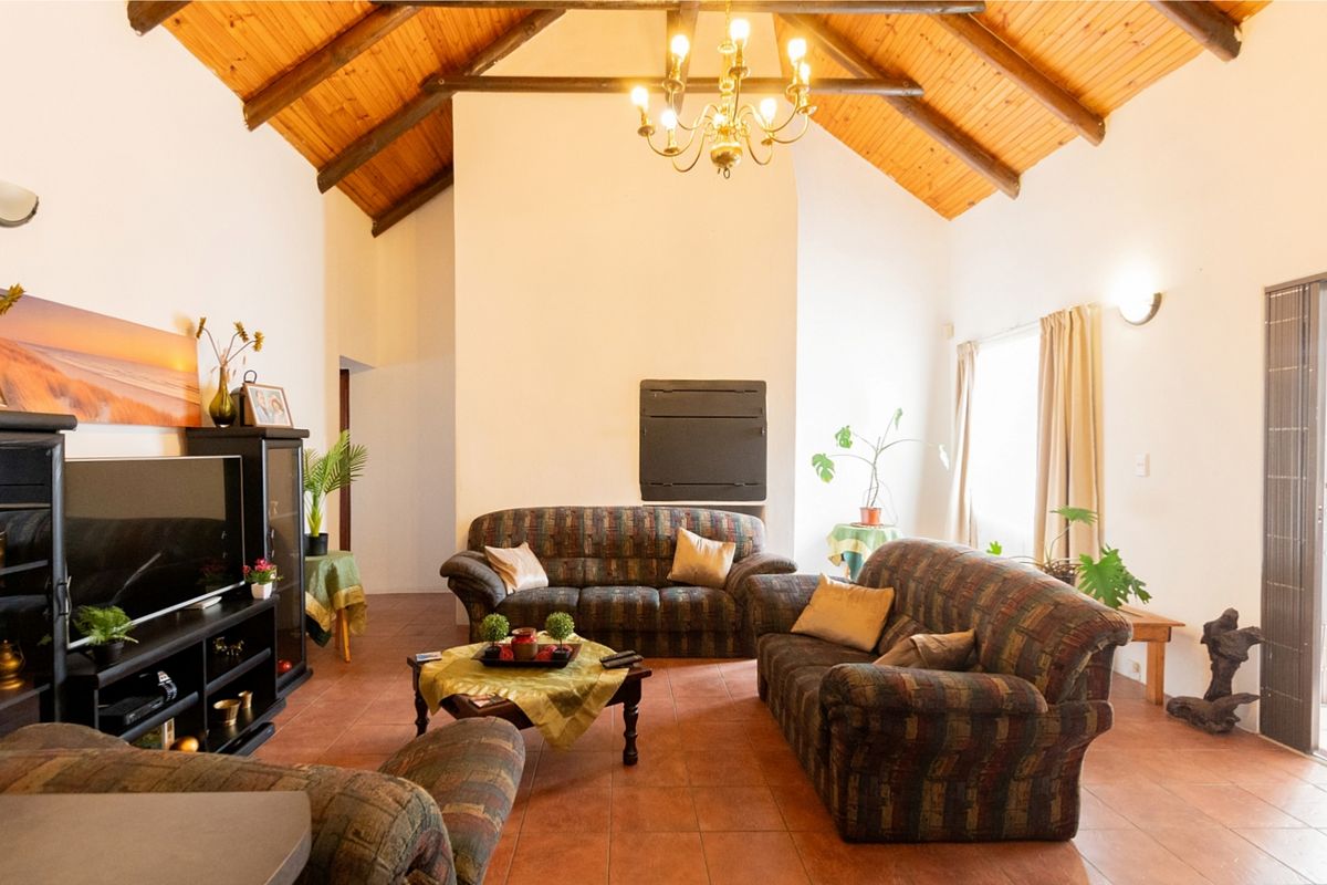 Spacious living room featuring a high vaulted timber ceiling with exposed beams, tiled flooring, and a central built-in fireplace.