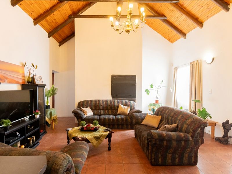 Spacious living room featuring a high vaulted timber ceiling with exposed beams, tiled flooring, and a central built-in fireplace.