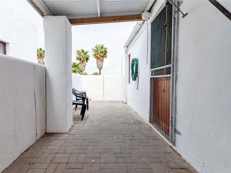 A covered outdoor patio area featuring paved flooring and a security gate, providing a functional space for outdoor relaxation.