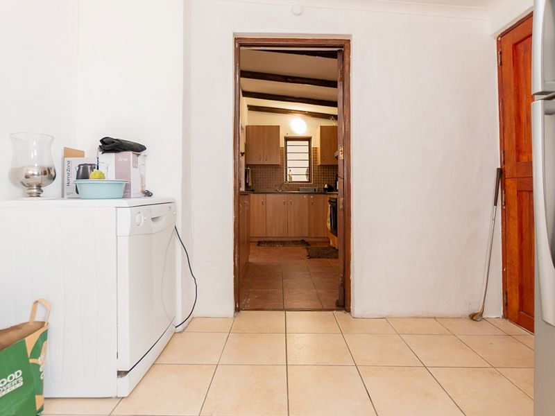 A functional laundry area with tiled flooring, leading through a doorway into a kitchen space featuring wooden cabinetry and exposed ceiling beams.