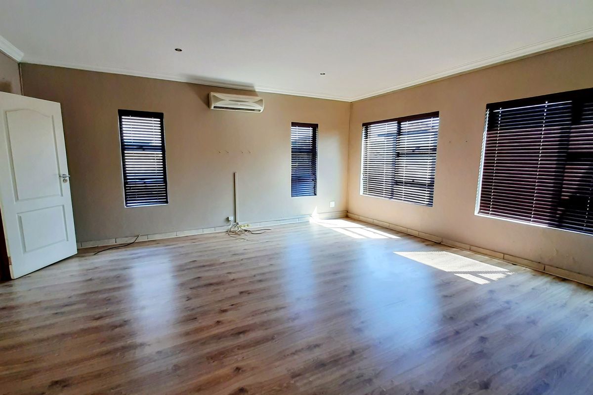 Spacious, empty living area featuring laminate flooring, split-system air conditioning, and large windows with fitted venetian blinds.