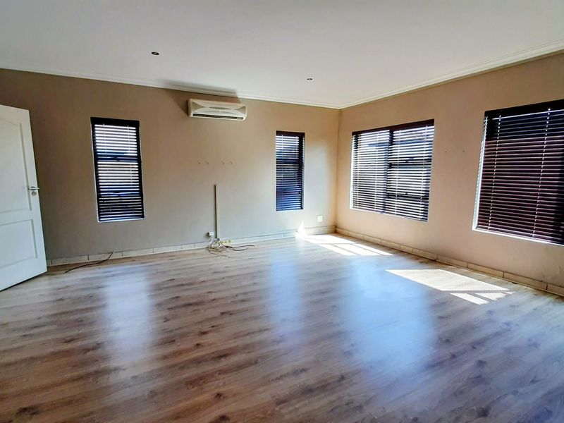 Spacious, empty living area featuring laminate flooring, split-system air conditioning, and large windows with fitted venetian blinds.