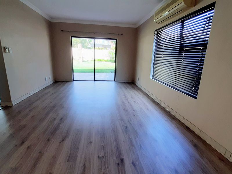 Spacious, empty living area featuring laminate flooring, a wall-mounted air conditioner, and sliding glass doors providing direct access to the garden.