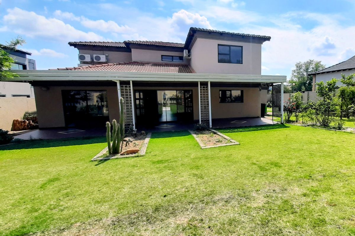 Rear view of a two-story house featuring a covered patio, sliding glass doors, and a well-maintained lawn and garden area.
