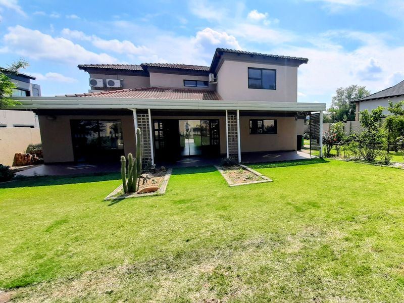 Rear view of a two-story house featuring a covered patio, sliding glass doors, and a well-maintained lawn and garden area.