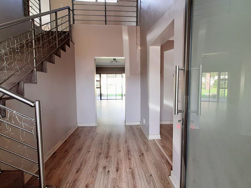 Spacious entrance hall featuring modern laminate flooring, a striking staircase with stainless steel balustrades, and a contemporary frosted glass front door.