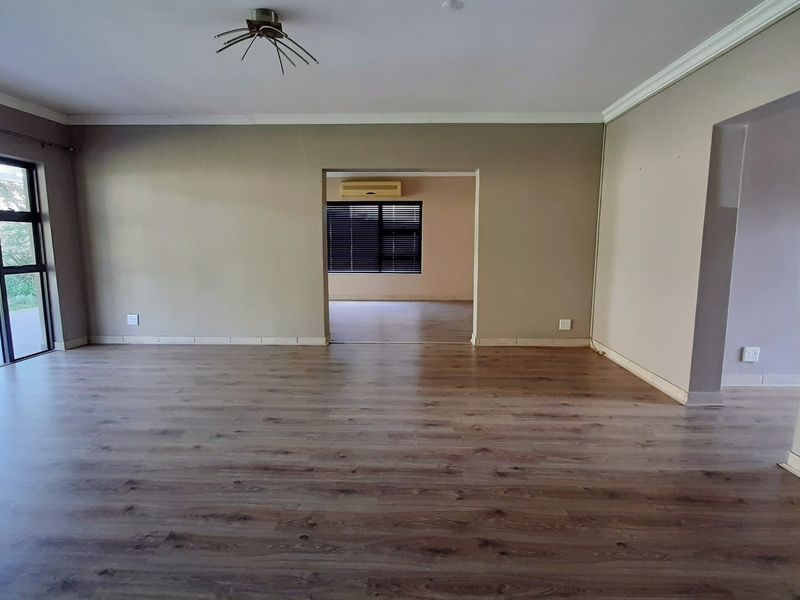 Spacious, empty living area featuring modern laminate flooring, neutral walls, and large sliding glass doors providing access to the outdoor patio area.
