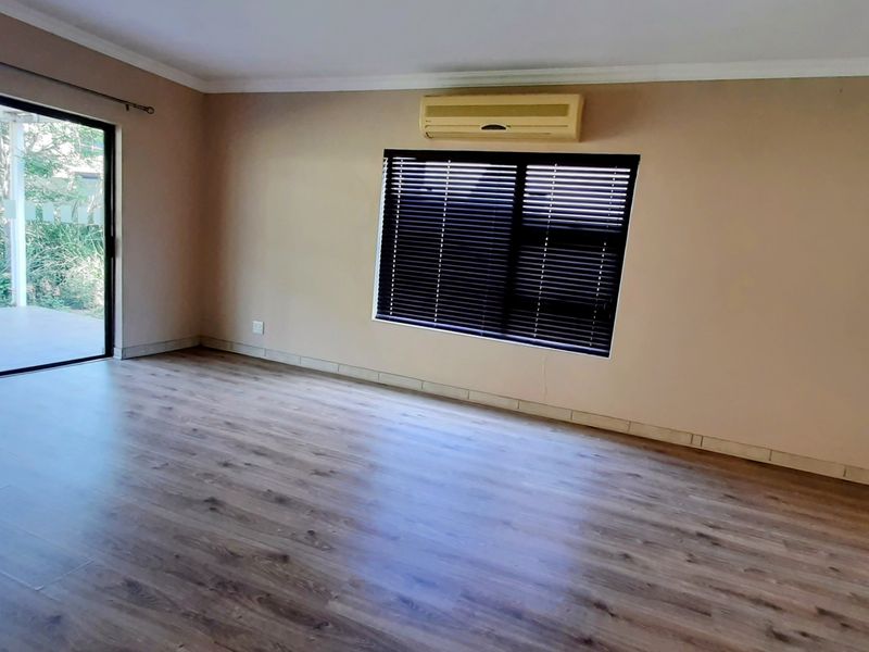 Spacious living area featuring laminate flooring, a split-system air conditioner, and large sliding glass doors providing access to the outdoor patio.
