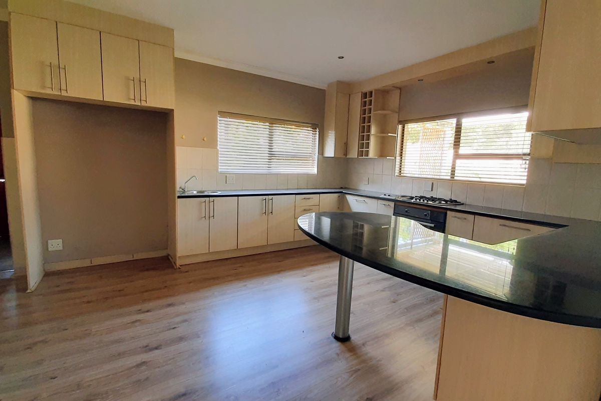 Spacious kitchen featuring light wood cabinetry, granite countertops, a breakfast bar, and integrated gas hob and oven, finished with modern laminate flooring.