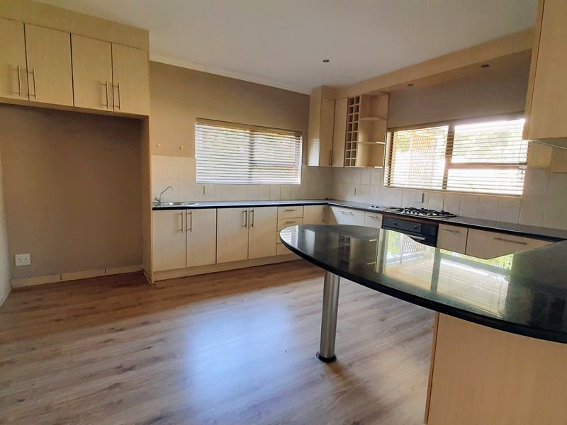 Spacious kitchen featuring light wood cabinetry, granite countertops, a breakfast bar, and integrated gas hob and oven, finished with modern laminate flooring.