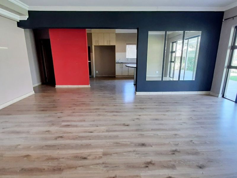 Spacious open-plan living area featuring modern laminate flooring, large glass sliding doors for natural light, and a view into the adjacent kitchen space.