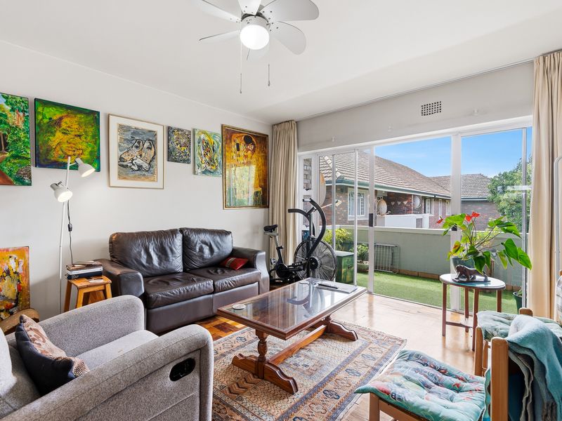 A bright living room featuring hardwood flooring, a ceiling fan, and large sliding glass doors that open onto a private balcony.
