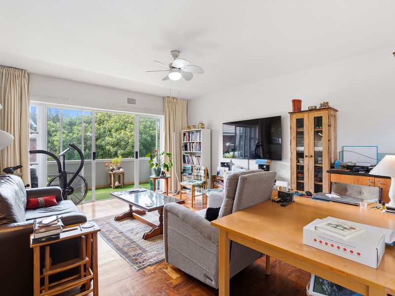 Spacious living room featuring warm parquet flooring, a ceiling fan, and large sliding glass doors that provide natural light and access to the balcony.