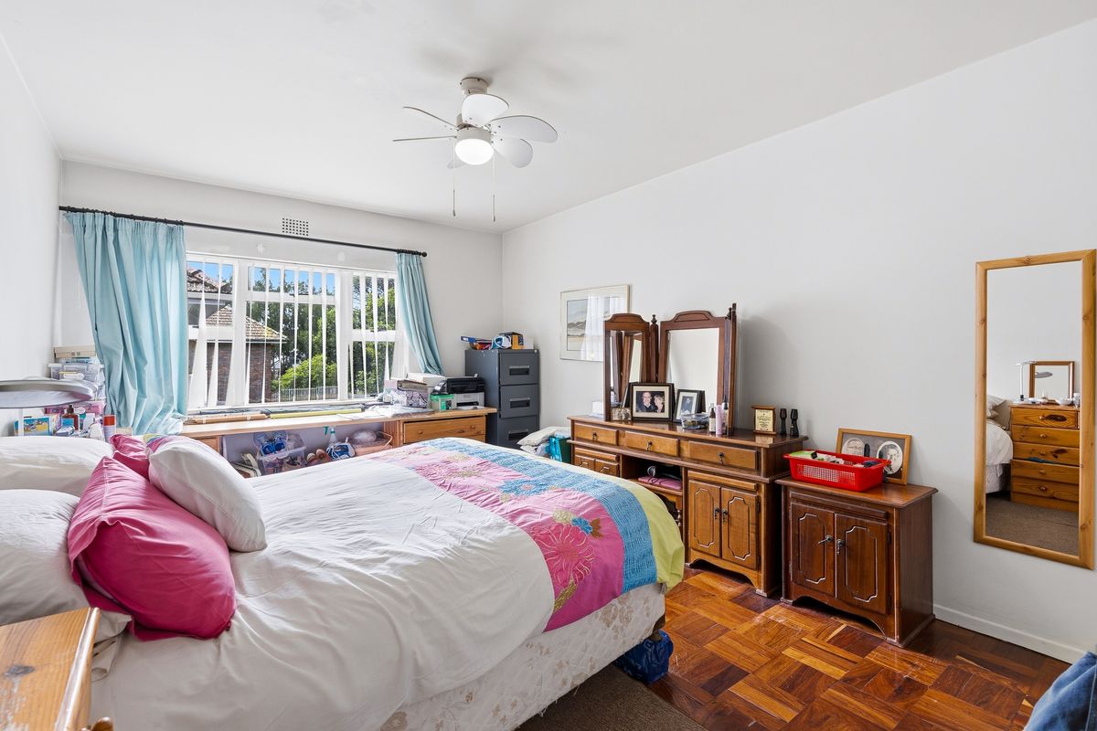A bedroom featuring classic parquet flooring, a ceiling fan, and large windows fitted with security bars for added peace of mind.