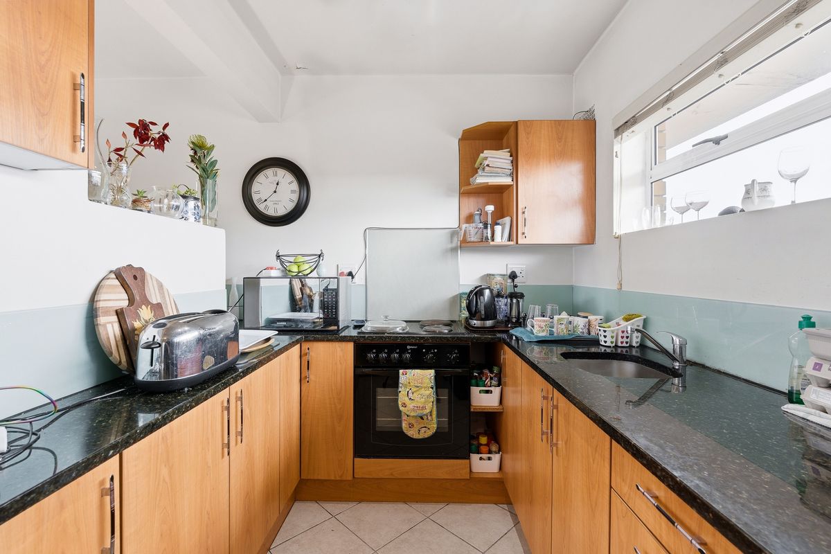A functional U-shaped kitchen featuring wood-finish cabinetry, dark granite countertops, a built-in oven, and a glass splashback with tiled flooring.