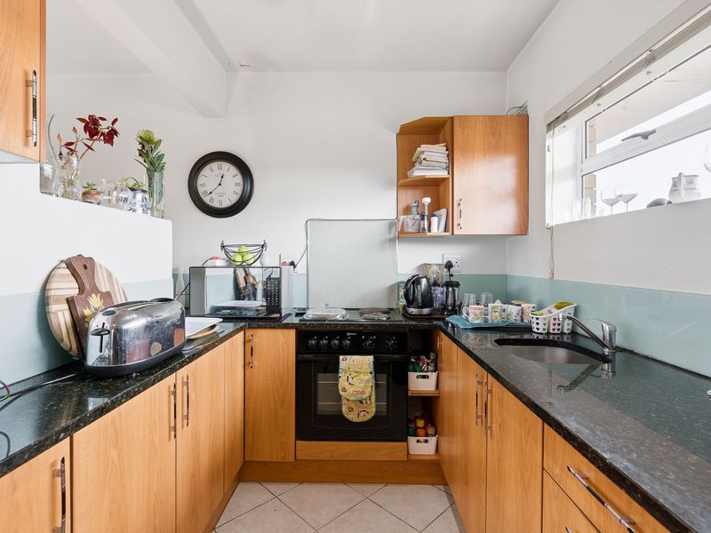 A functional U-shaped kitchen featuring wood-finish cabinetry, dark granite countertops, a built-in oven, and a glass splashback with tiled flooring.