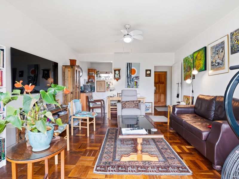 A well-lit living room featuring classic parquet flooring, a central ceiling fan, and a solid timber entrance door.