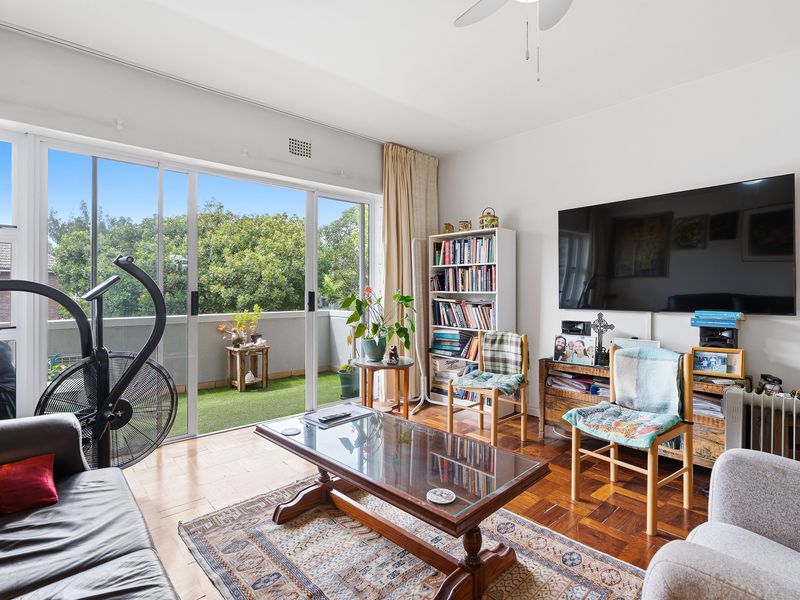 A bright living room featuring classic parquet flooring and large sliding glass doors that open onto a private balcony with green views.