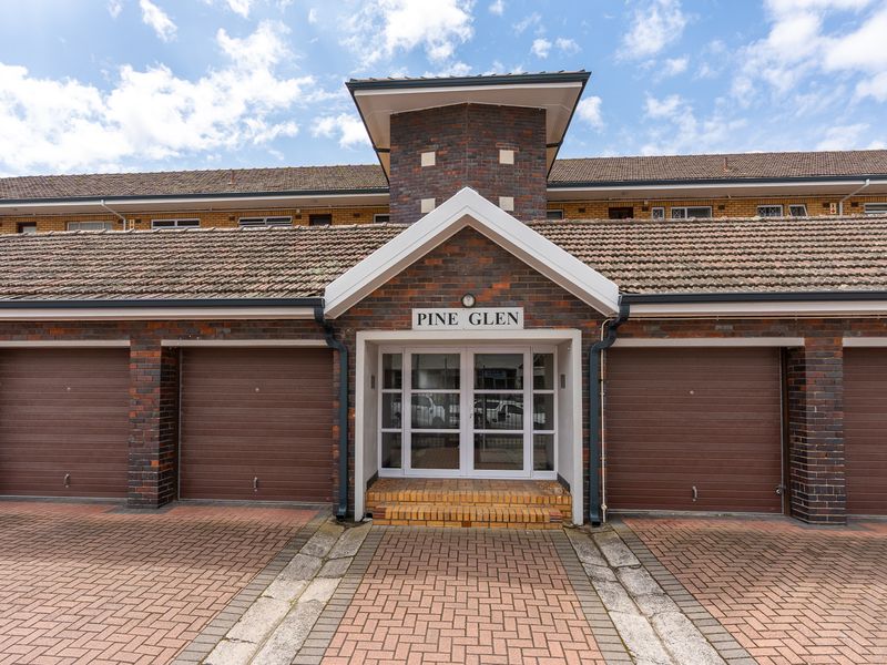 Front elevation of Pine Glen apartment complex featuring a brick facade, tiled roof, multiple garage doors, and a central glass entrance.