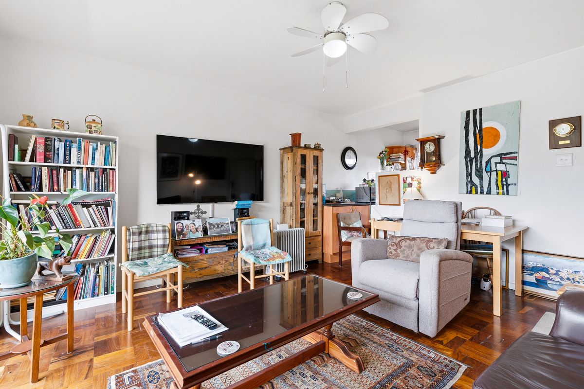 A comfortable living room featuring classic parquet flooring and a ceiling fan, offering a warm and inviting space for relaxation.