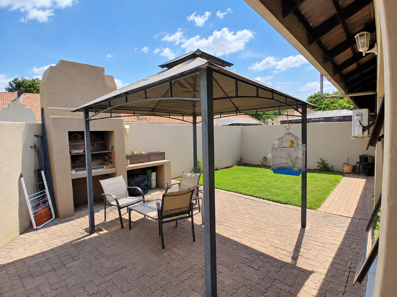 A paved outdoor patio area featuring a built-in braai, covered by a gazebo, adjacent to a small private garden and perimeter wall.