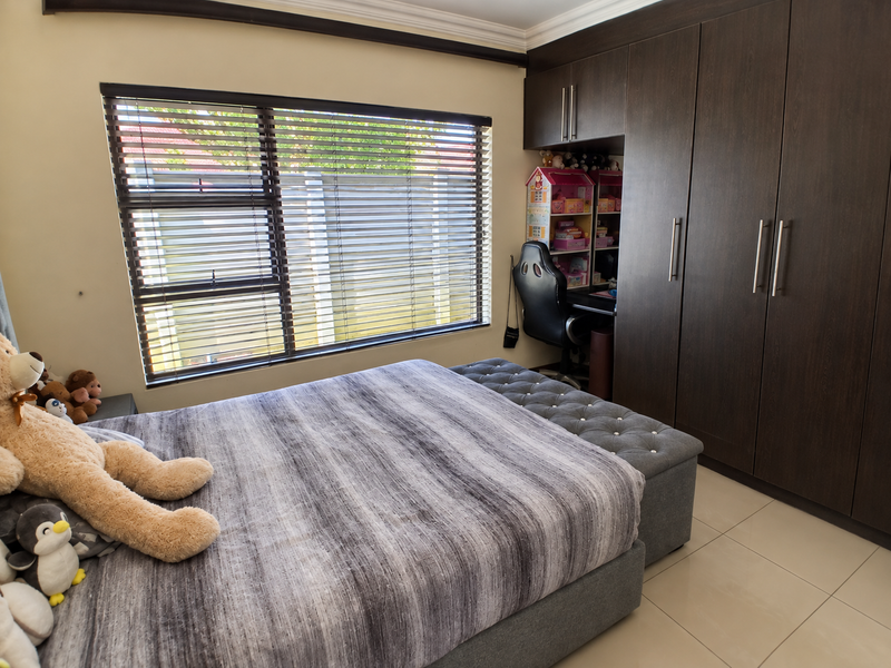 A well-maintained bedroom featuring dark wood built-in cupboards, a integrated desk area, tiled flooring, and venetian blinds.