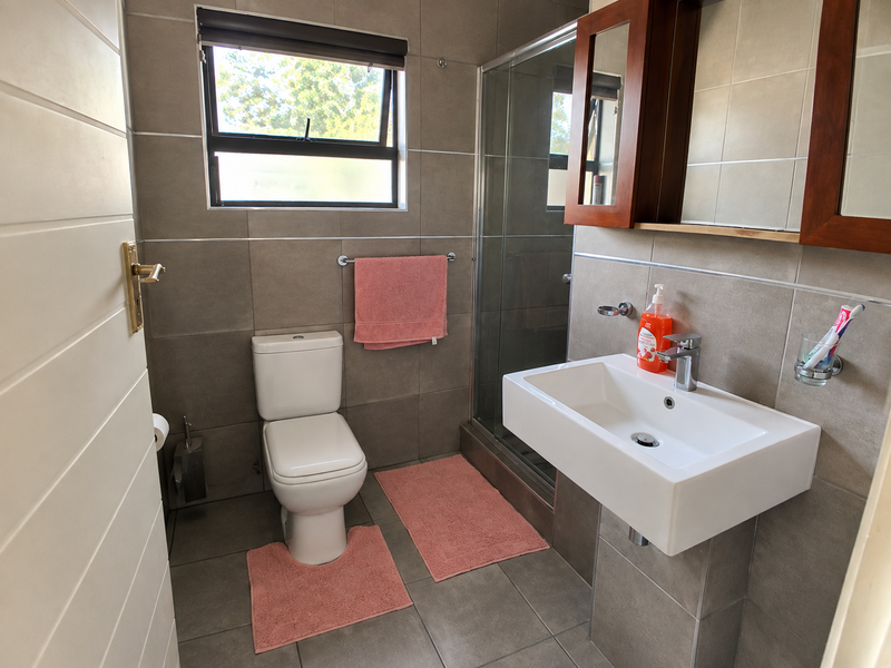 A modern bathroom featuring a wall-mounted basin, glass shower enclosure, and neutral floor-to-ceiling tiling.