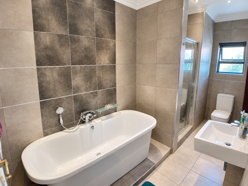 Modern bathroom featuring a freestanding bathtub, glass-enclosed shower, wall-hung toilet, and contemporary basin with neutral-toned ceramic tiling throughout.