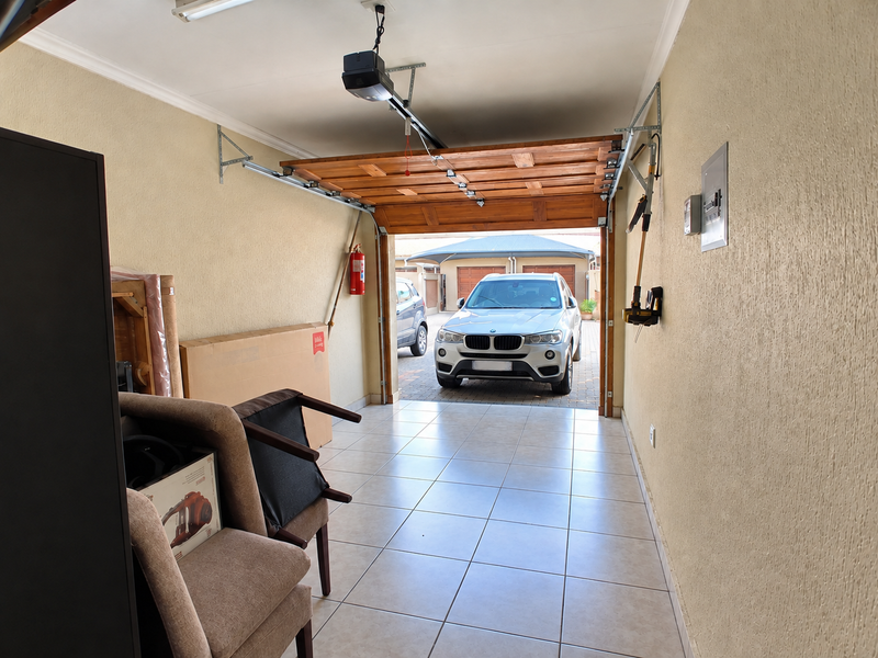 A clean, tiled garage featuring an automated door system, wall-mounted fire extinguisher, and an accessible electrical distribution board.