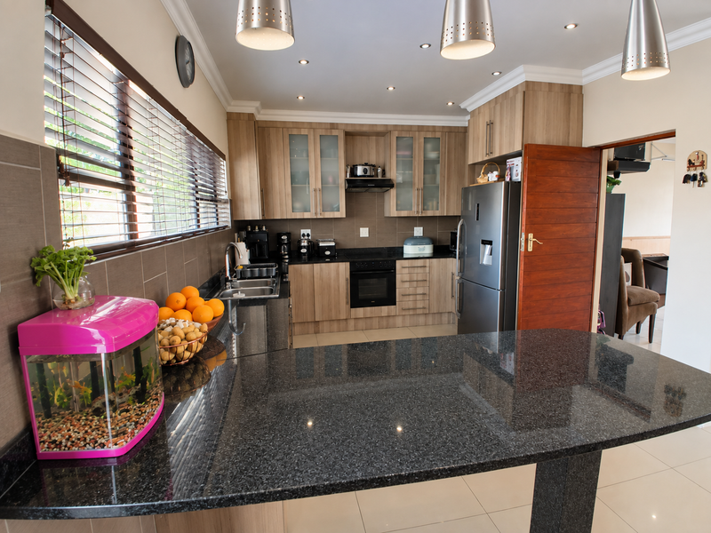 Modern kitchen featuring granite countertops, wooden cabinetry, built-in oven, hob, extractor fan, and tiled flooring with ample workspace and recessed lighting.