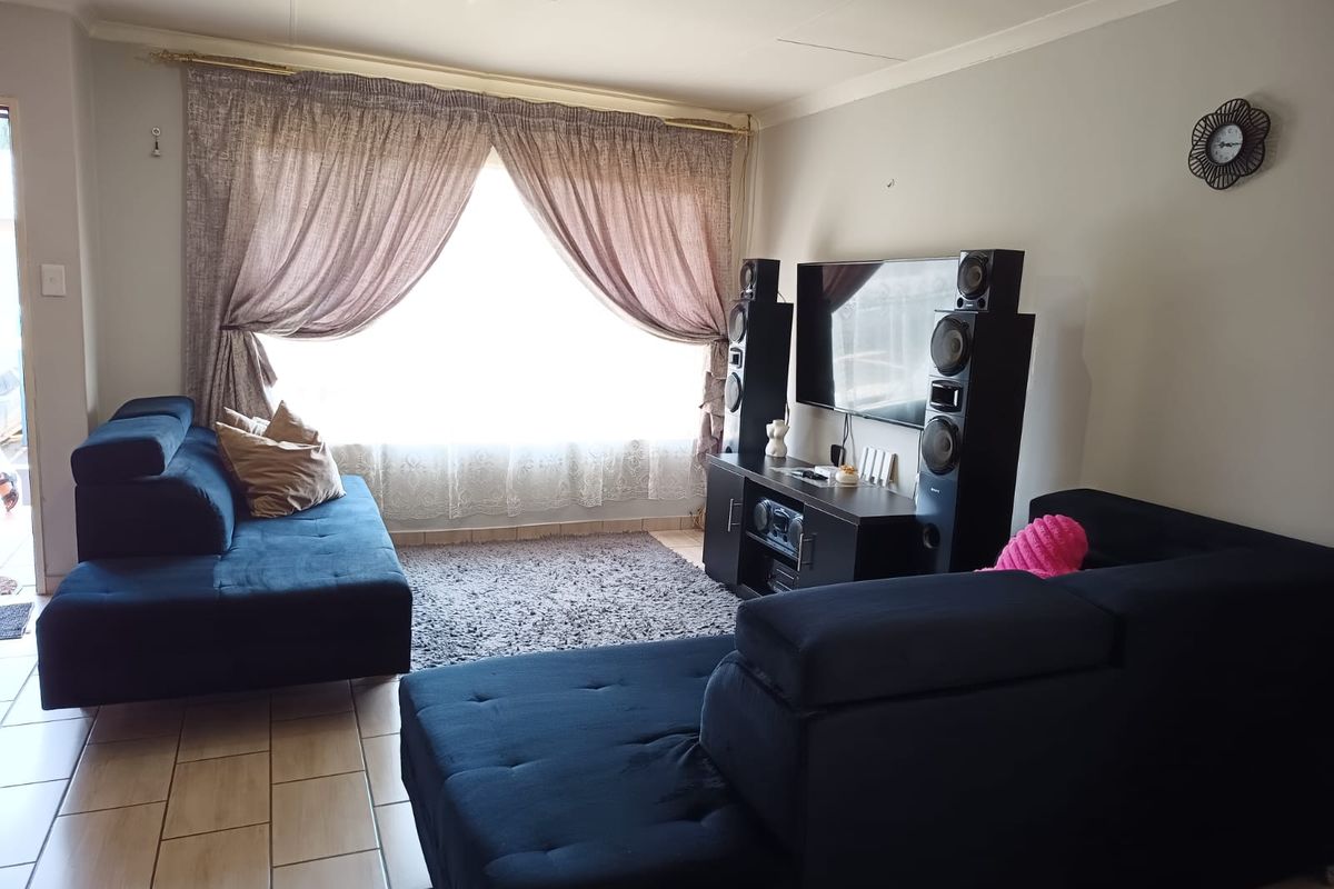 A comfortable living room featuring tiled flooring and a large window with curtain treatments, providing a functional and well-lit space.