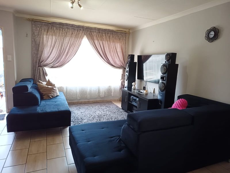 A comfortable living room featuring tiled flooring and a large window with curtain treatments, providing a functional and well-lit space.