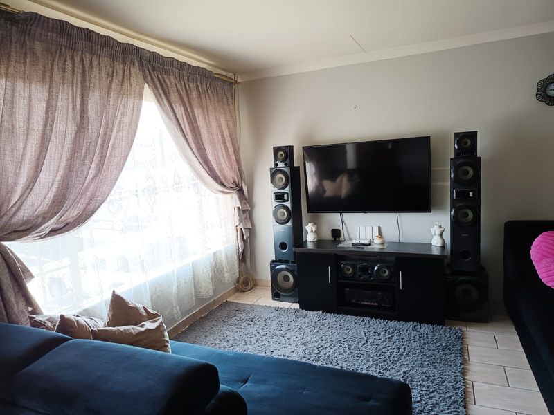 A comfortable living room featuring tiled flooring and large windows with curtain rails, providing a bright and functional space for relaxation.