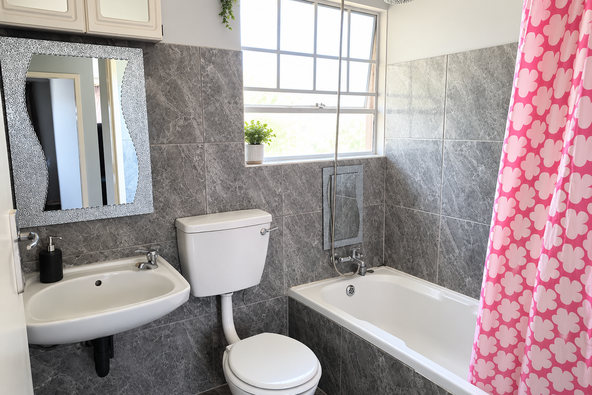 A functional bathroom featuring grey marble-effect wall tiles, a wall-mounted basin, a standard toilet, and a bathtub with an overhead shower fixture.