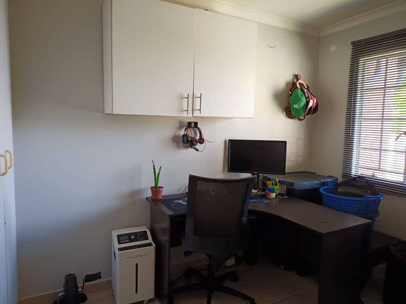 A functional home office space featuring wall-mounted storage cabinetry, tiled flooring, and natural light provided by a window with venetian blinds.