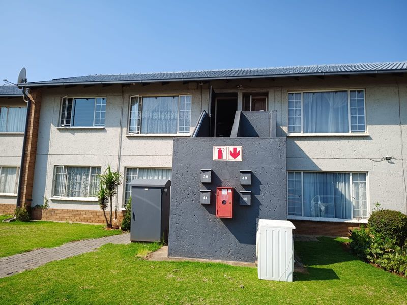 Front elevation of a multi-story apartment complex featuring a tiled roof, metal-framed windows, and communal post boxes set within a landscaped garden area.