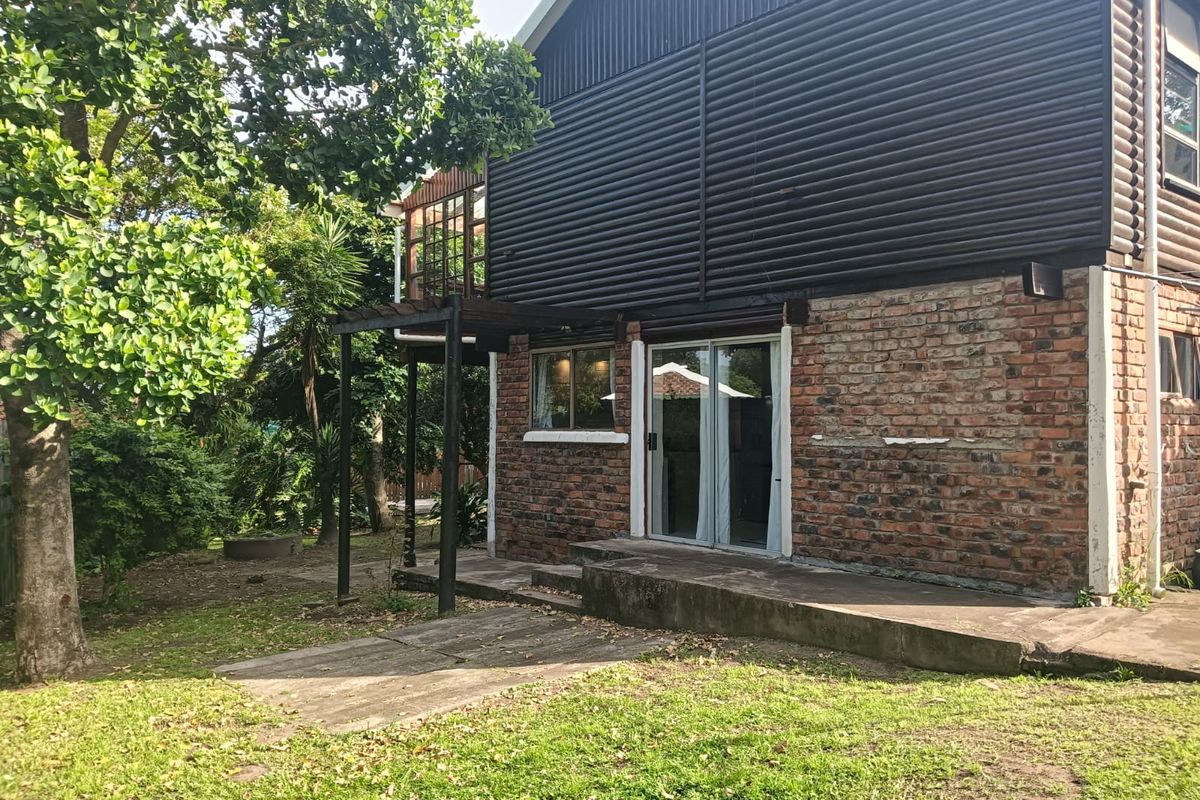 Rear view of the house featuring a brick and corrugated metal facade, a concrete patio, and a timber pergola overlooking the garden.