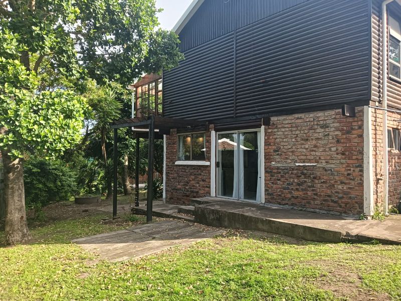 Rear view of the house featuring a brick and corrugated metal facade, a concrete patio, and a timber pergola overlooking the garden.