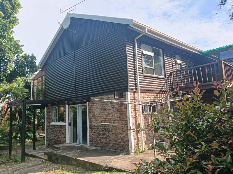 Rear view of a two-story house featuring a combination of brick and timber cladding, a concrete patio, and an elevated timber balcony.